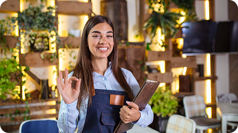 Mujer administradora de restaurante sonriendo mientras usa tecnología digital para gestionar reservas y atención al cliente, representando el sistema automatizado de Risto Suite.